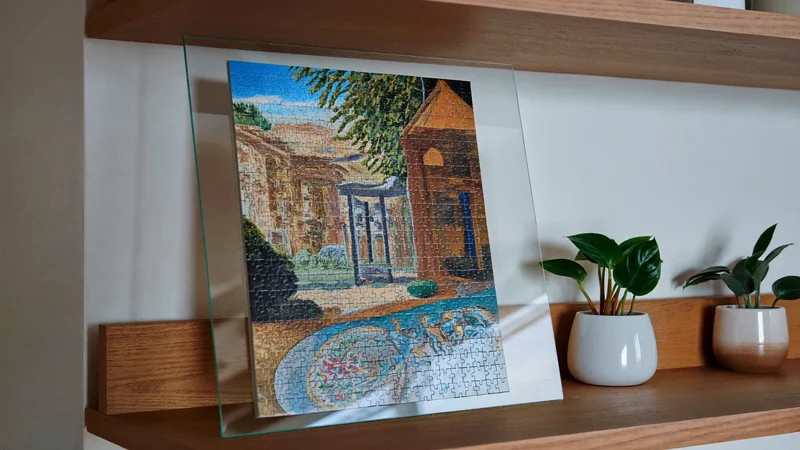 Puzzle terminé monté sous verre et posé sur une étagère avec des plantes